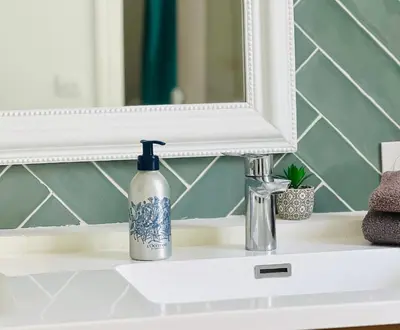 a bottle of soap on a bathroom sink in front of a mirror at Superbe Appartement de 105 m2, hyper centre avec Terrasse, parking, à 5 min de la mer in Nice