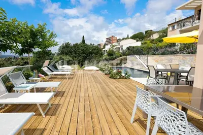 a wooden deck with chairs and tables and a pool at Villa Vue Mer, Piscine & Plage à 6Min in Cagnes-sur-Mer