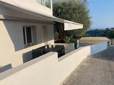 a white house with a black table and an umbrella at Superbe appartement au calme et vue sur la mer in Cagnes-sur-Mer
