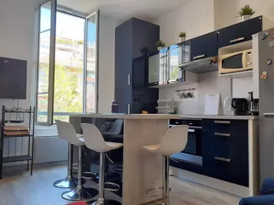 a kitchen with black cabinets and white stools at 2 Pièces Neuf WIFI Quartier Borriglione in Nice