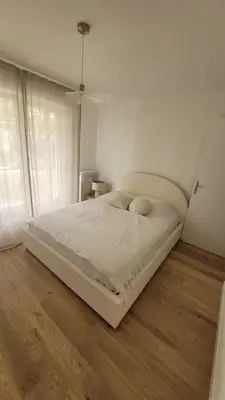 a bed in a white bedroom with a wooden floor at Magnifique appartement Bas Gairaut aperçu mer in Nice