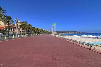a boardwalk on a beach with palm trees and buildings at Accès direct Promenade Des Anglais - Negresco in Nice