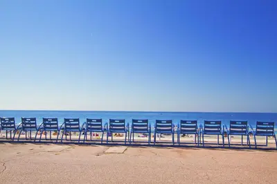 a row of blue chairs sitting on the beach at Sea Front Palace Promenade in Nice