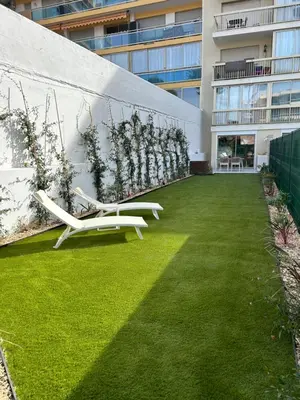 a garden with two white benches on the side of a building at Riviera 1 ou Riviera 2 ou réservez les 2 Front de Mer Cagnes sur Mer Promenade de la plage in Cagnes-sur-Mer