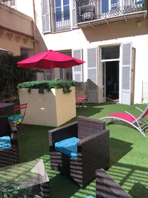 a patio with chairs and an umbrella on the grass at Superbe 2 pièces Carré d’or avec grande Terrasse in Nice