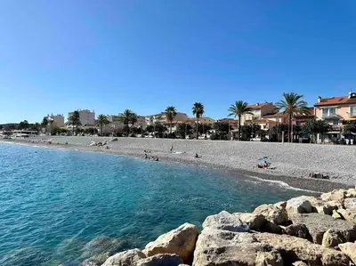 a beach with people laying on the sand and rocks at Orangers - Bord de mer - Studio cosy 4 personnes in Cagnes-sur-Mer