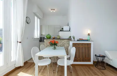 a white kitchen with a table and white chairs at Deux pièces terrasse sous les étoiles in Nice
