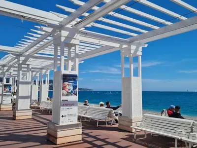 people sitting on benches on a boardwalk near the beach at Villa Reine - Nice in Nice