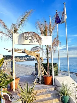 a sign on a beach with palm trees and the ocean at La Tanière du Bois Flotté in Nice