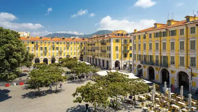 a group of yellow buildings in a square with trees at Elegant mansardé-place du pin in Nice