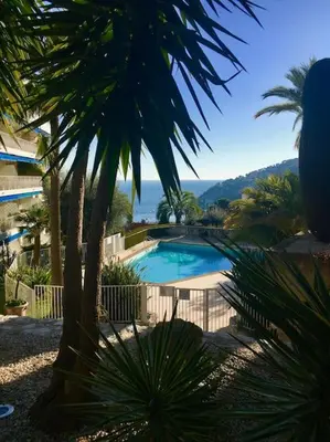 a swimming pool with a palm tree and a fence at Appartement „Bellevue“ Villefranche-sur-Mer in Villefranche-sur-Mer