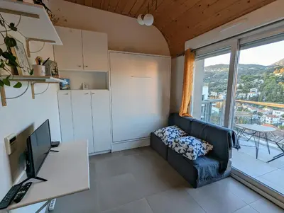a living room with a couch and a desk with a television at Studio calme avec vue dégagée in Nice