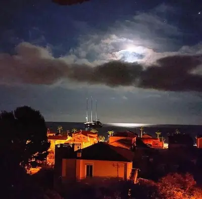 a view of a city at night with a boat in the distance at Sea View Apartment - Private Parking, Swimming Pool, Air Conditioning in Cagnes-sur-Mer
