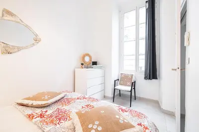 a white bedroom with a bed and a chair at La Petite Chaise Bleue Appartement classe 3 etoiles in Nice
