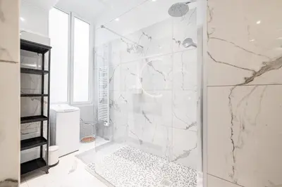 a white bathroom with a shower with marble walls at La Petite Chaise Bleue Appartement classe 3 etoiles in Nice
