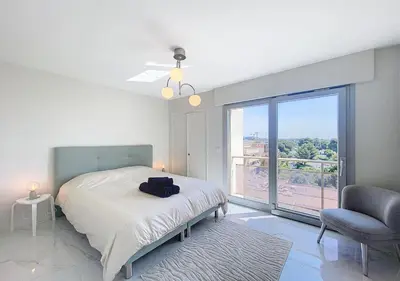 a bedroom with a bed and a chair and a large window at Horizon bleu vue mer dernier étage clim in Saint-Laurent-du-Var