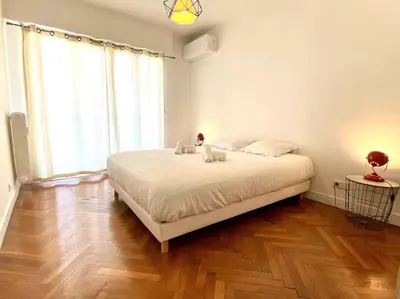 a white bedroom with a large bed and a wooden floor at Large flat terrace Sea view, Promenade des Anglais in Nice