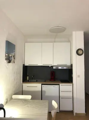 a kitchen with white cabinets and a table and a clock at Le Rabelais, Studio terrasse in Nice