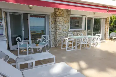 a patio with white tables and chairs and a stone wall at Appartement exception les pieds dans l'eau in Èze