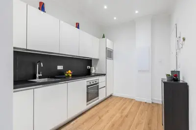 a white kitchen with white cabinets and a wooden floor at Center 2 min walk to beach quiet sunny balcony in Nice