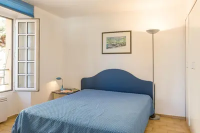 a bedroom with a blue bed and a window at Résidence Partenaire Le Palais de la Marine in Villefranche-sur-Mer