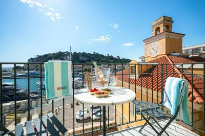 a balcony with a table and a clock tower at Sunlight Properties - Capitaine 54 - 1 Bedroom, stunning holiday rental apartment with balcony and port view in Nice