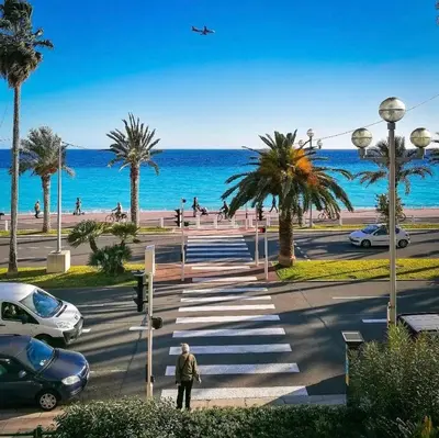 a man walking down a street near the ocean with an airplane at Le Grand Palais de la Méditerranée Beach Access Apartments - Top Choice In Nice in Nice