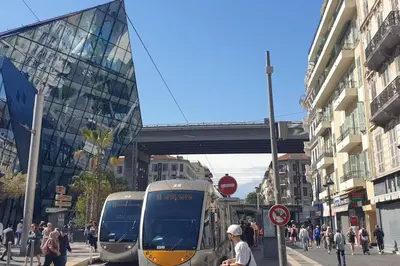 two trains on a city street with people and buildings at Studio Emmé neuf indépendant Nice Centre in Nice
