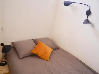 a bed with an orange pillow and two lamps at Appartement proche de Libération avec balcon ensoleillé in Nice