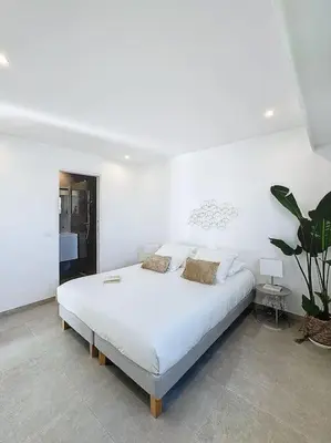 a white bedroom with a white bed and a plant at Évasion Mer & Vue Imprenable in Saint-Laurent-du-Var