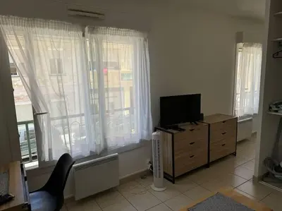 a living room with a television on a dresser with windows at Studio lumineux in Nice