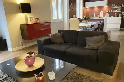 a living room with a black couch and a kitchen at Appartement 2 chambres à 15 mn de la mer in Nice