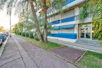 a sidewalk next to a building with palm trees at Cosy 2P Promenade des Anglais in Nice