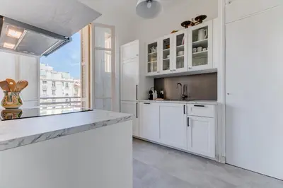 a kitchen with white cabinets and a large window at Elegant Condo with Balconies in the Heart of Nice in Nice
