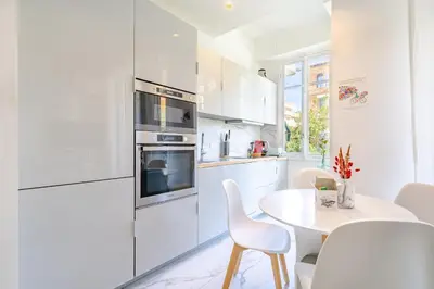 a white kitchen with a table and white chairs at Charmant 2P au cœur de Nice in Nice