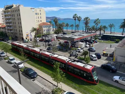 a red train traveling down a city street with cars at Nizza-Azur vue mer in Nice