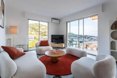 a living room with white furniture and large windows at LE SAINT ESTEVE AP4435 By Riviera Holiday Homes in Villefranche-sur-Mer