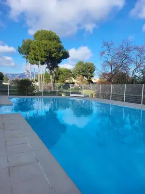 a blue swimming pool with trees in the background at Maison entre mer et montagnes in La Gaude