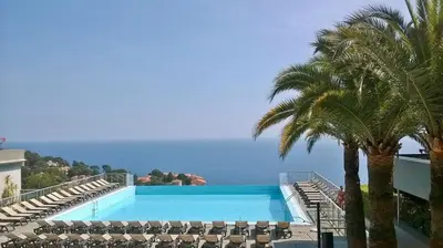 a large swimming pool with palm trees and the ocean at Appartement Zen Costa Plana in Cap d'Ail