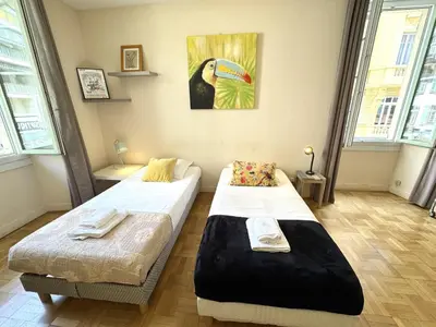 two beds in a room with a bird painting on the wall at ApartHotel Riviera - Hotel des Postes 2 - City center Massena in Nice