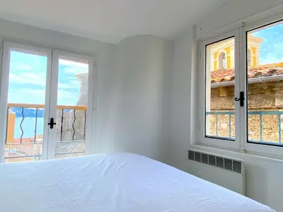 a white bedroom with a bed and two windows at PERCHOIR AP4443 By Riviera Holiday Homes in Villefranche-sur-Mer