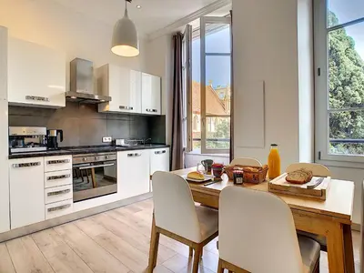 a kitchen with white cabinets and a wooden table and chairs at Nestor&Jeeves - COTE JARDIN - Central - Close sea in Nice