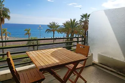 a wooden table and chairs on a balcony with the ocean at Charming T1 with terrace and sea view in Nice