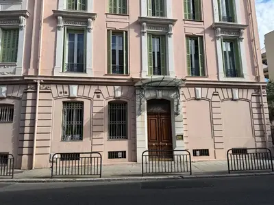 a pink building with benches in front of it at Appartement 3 pièces 5 min plage in Beaulieu-sur-Mer