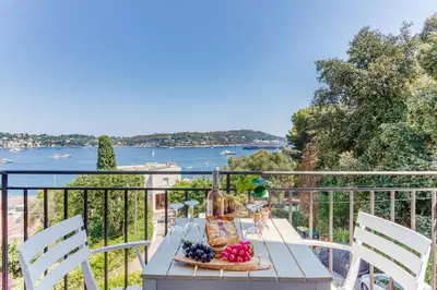 a table on a balcony with a view of the water at BELLE DARSE AP4454 By Riviera Holiday Homes in Villefranche-sur-Mer