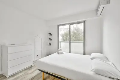 a white bedroom with a bed and a window at Flat with balcony 15min from Promenade des Anglais in Nice