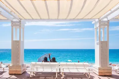 two women sitting on a bench at the beach at FLEUR- Cosy Studio, 200 Promenade des Anglais et Negresco, wifi, climatisation- calme in Nice