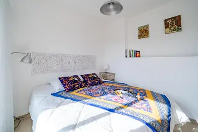 a white bedroom with a bed with a colorful comforter at 2 pièces Calme Proche de la mer Parking en sous-sol in Cagnes-sur-Mer