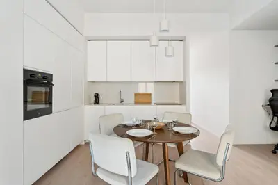 a white kitchen with a wooden table and chairs at Appartement Ostave - Welkeys in Nice