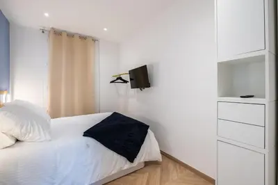 a white bedroom with a bed and a tv on the wall at Design Apartment near the Beaches of Nice in Nice